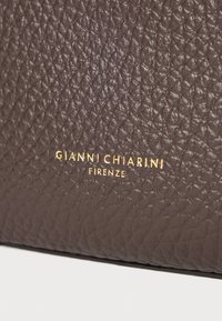 Brązowa skórzana powierzchnia o teksturze, na której widnieje wyraźnie wytłoczone na złoto logo z napisem "GIANNI CHIARINI FIRENZE."