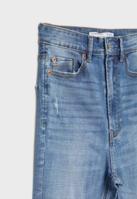 Super vysoké modré džíny z denimu s jemným blednutím, bronzovými nýty a jednou přední kapsou. Texturovaná látka s oranžovými švy.