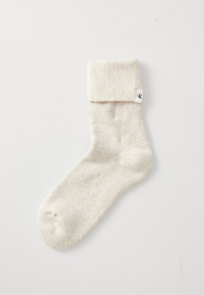 Bežna nogavica z rebrastim robom, izdelana iz mehkega materiala, z diskretno teksturo in majhno oznako na strani.