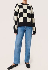 Schwarz-weiß kariertes Strickoberteil mit geripptem Ausschnitt und Bündchen, kombiniert mit hellblauen geraden Jeans und schwarzen Ballerinas.