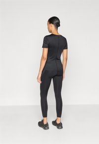 Μαύρο αθλητικό τοπ με κοντά μανίκια, εφαρμοστή σχεδίαση, κομψή υφή, σε συνδυασμό με μαύρο κολάν και υφασμένο μαύρο παπούτσι.