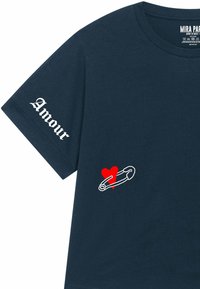 T-shirt en coton bleu marine avec le texte "Amour" en blanc, et un cœur rouge à côté d'un graphique d'épingle de sûreté blanche sur le devant.