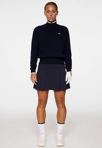 Maglione blu navy con collo a mezza zip, abbinato a una gonna plissettata blu navy. Calzini bianchi e guanto, con calzature leggere. Design semplice e pulito.