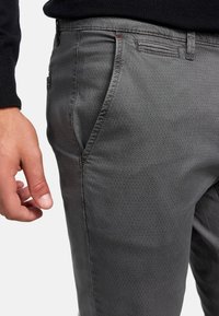 Pantalons gris à motif avec une texture lisse et une coupe slim. Comprend une petite poche et des coutures fines le long des coutures.