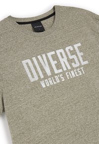 Olive zielona bawełniana koszulka z krótkim rękawem, z białym nadrukiem "DIVERSE WORLD'S FINEST" na przodzie. Metka wskazuje rozmiar L.