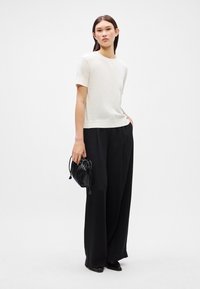 Camiseta clara con cuello redondo, combinada con pantalones negros anchos y un pequeño bolso negro. Textura de tela suave, diseño minimalista.