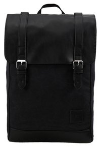 Sac à dos noir avec un corps en toile et un rabat en cuir, des bretelles réglables, des boucles en métal et un petit patch logo sur le devant.