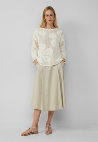 Leichter Strickpullover in Elfenbein mit offener Maschenstruktur und Blattmustern, kombiniert mit einem fließenden beigen Rock und Sandalen mit Riemchen.