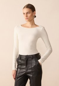 White, ribbed long-sleeve top with a boat neckline, paired with high-waisted black leather pants featuring front pockets and seam detailing.