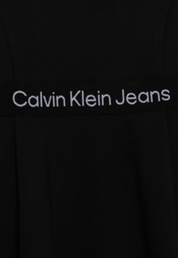 Czarna bawełniana odzież z szeroką elastyczną tasiemką z białym napisem "Calvin Klein Jeans". Gładka tekstura z minimalistycznym designem.
