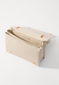 Béžová kožená kabelka se strukturovaným designem, obsahující dvě vnitřní přihrádky a zlaté kovové detaily. Hladký povrch a minimalistický styl.