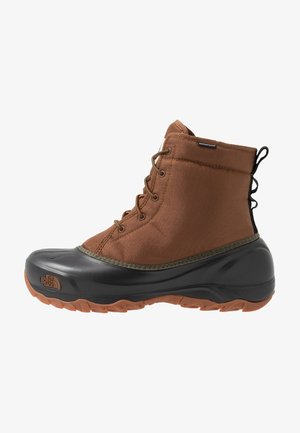 Botte d’hiver marron imperméable à lacets avec partie inférieure en caoutchouc noir, semelle robuste et languette au talon pour une utilisation extérieure.