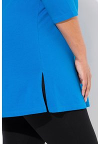 Blauwe katoenen top met korte mouwen, met een split aan de zijkant en een rechte zoom. Gecombineerd met zwarte leggings. Gladde textuur.