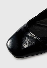 Black patent leather flat shoe with a square toe, featuring a textured upper and smooth interior lining.