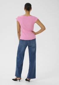 Rosa geripptes Oberteil mit kurzen, gerafften Ärmeln, kombiniert mit lockeren blauen Denim-Jeans und schwarzen Mules mit Kitten-Absätzen, von hinten betrachtet.