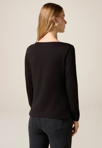 Czarna bluzka z długim rękawem i okrągłym dekoltem, wykonana z gładkiego materiału. Charakteryzuje się prostym designem, bez wzorów i ozdób.