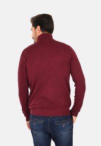 Maglione a collo alto bordeaux realizzato in morbido tessuto a maglia, con colletto e orlo a coste, abbinato a jeans blu scuro.