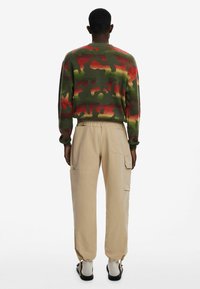 Sweater in groene camouflage met rode en oranje accenten; gecombineerd met beige cargobroek met meerdere zakken en elastische manchetten.