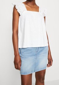 Hvid, let, ærmeløs top med firkantet halsudskæring og blonderkanter. Kombineret med en tætsiddende, lyseblå denim mininederdel.