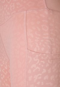 Růžové legíny vyrobené z měkkého, elastického materiálu s jemným leopardím vzorem, se šitými švy a boční kapsou.