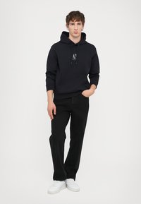 Marineblaue Kapuzenjacke mit Kordelzügen und Fronttasche; kombiniert mit schwarzen Jeans im geraden Schnitt und weißen Sneakers. Einfaches Design, Mischgewebe aus Baumwolle.