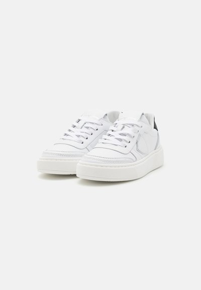 Baskets en cuir blanc avec une texture lisse, semelle plate en caoutchouc blanc, design cousu, bout rond, et accents noirs contrastants au niveau du talon.