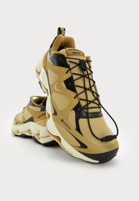 Zapatillas de deporte para exterior en beige y negro, con parte superior de malla, marca GORE-TEX, suela gruesa y líneas de diseño audaces.