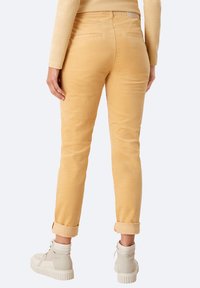 Pantaloni in corduroy gialli con una vestibilità affusolata, orli arrotolati e tasche posteriori, abbinati a sneakers beige alte. Texture liscia e leggero lucido.