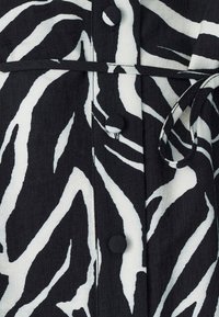 Schwarz-weiß gestreifter Stoff im Zebramuster mit strukturierter Oberfläche, versehen mit runden Knöpfen und einer gebundenen Gürtel-Detail an der Taille.