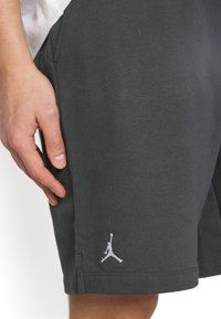 Gros plan sur la main d'une personne reposant près de la poche d'un short noir avec un petit logo Jumpman blanc près de l'ourlet.