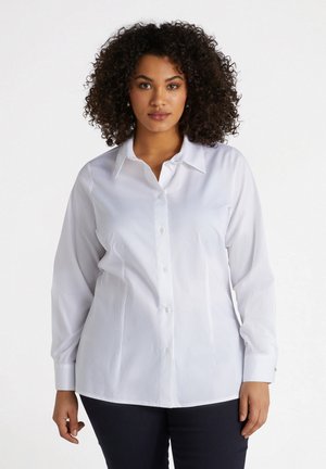 Camisa blanca de botones hecha de una tela suave con cuello clásico, mangas largas y puños abotonados, exhibida en un modelo.