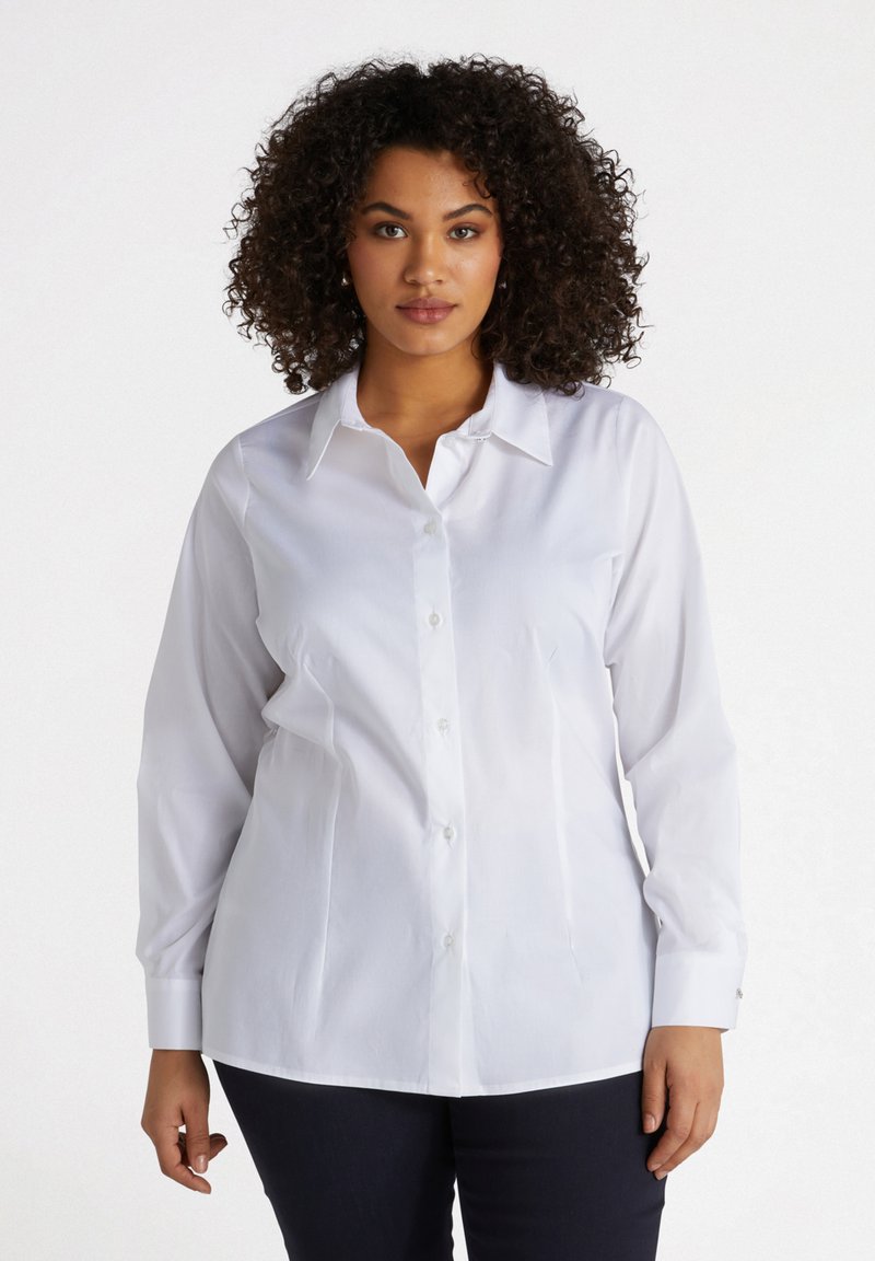 Camicia bianca con bottoni realizzata in un tessuto morbido, con colletto classico, maniche lunghe e polsini con bottoni, indossata da un modello.