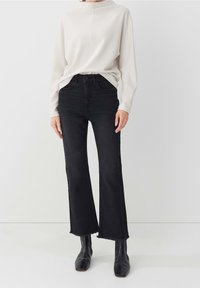 Black high-waisted jeans with a flared leg and raw hem, paired with a light beige textured long-sleeve top and black ankle boots.