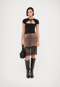 Μαύρο εφαρμοστό τοπ με άνοιγμα σε σχήμα κλειδιού, συνδυασμένο με φούστα λεοπάρ με μαύρο δαντελένιο τελείωμα. Το μοντέλο έχει αξεσουάρ με μαύρη τσάντα και μπότες.