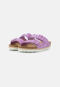 Purple suede sandals with two adjustable straps, cork footbed, and white rubber outsole; features a textured surface and buckle accents.