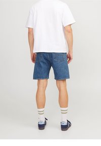 Jeansshorts i mellanblått med en klassisk passform, tillsammans med en vit T-shirt, vita strumpor med gröna ränder och marinblå skor.