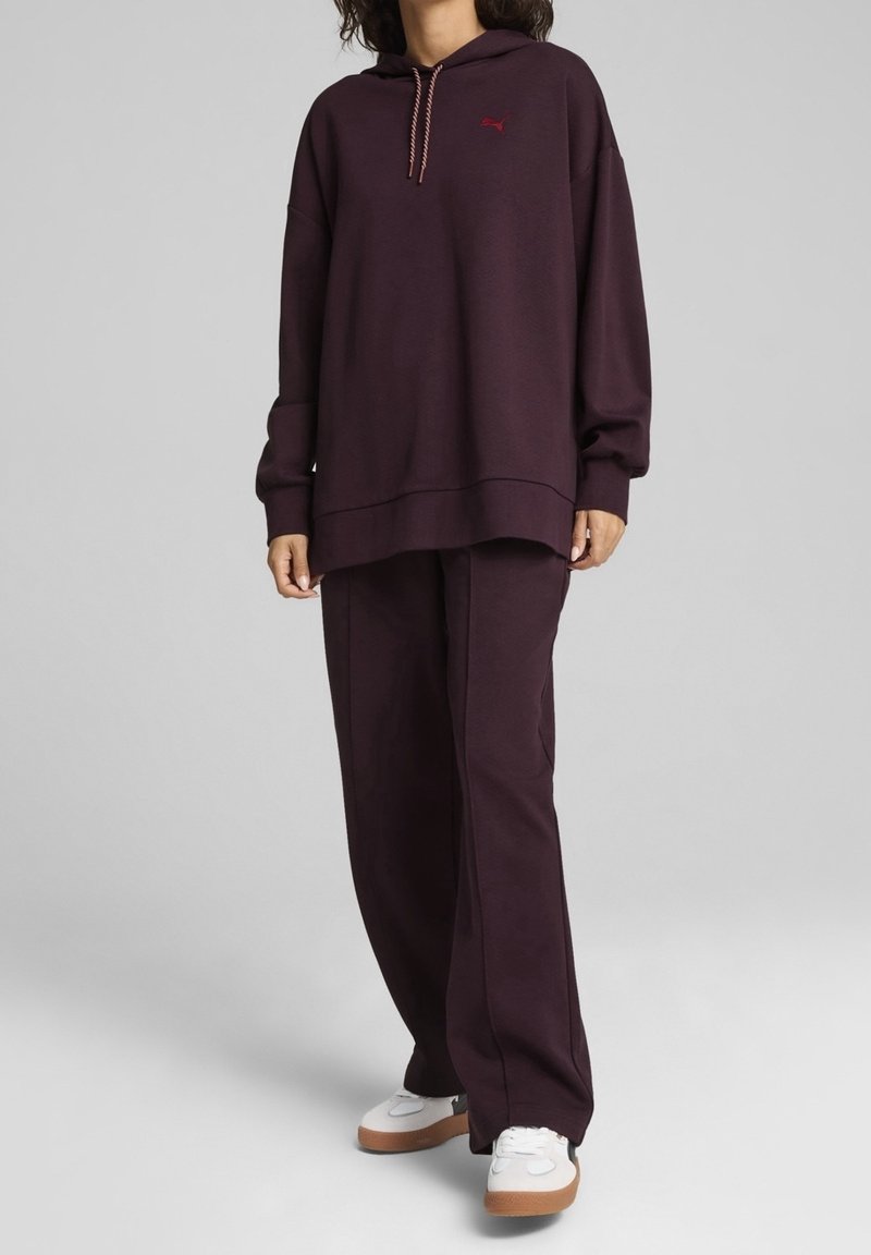 Felpa con cappuccio Puma di colore viola scuro e pantaloni coordinati, dotati di tasca frontale, coulisse e sneakers bianche con suola in gomma.