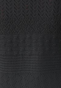 Černá pletenina s texturovanými vzory, kombinující otevřené a uzavřené stehy, vytvářející kontrastní design a různorodou povrchovou texturu.