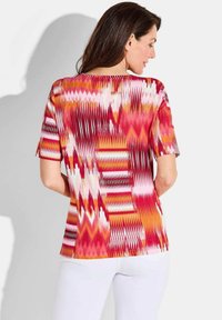 Korte mouwen top met een kleurrijk zigzagpatroon in tinten roze, rood en oranje, gemaakt van een zachte, gestructureerde stof.