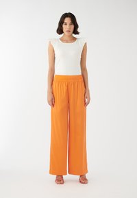 Vit linne med volangärmar, matchat med vida orange byxor. Outfiten har en avslappnad passform och en mjuk textur.