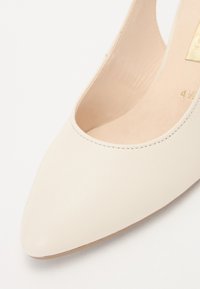 Beige nahkapohjalliset korkokengät, joissa on terävä kärki, matalareunaiset sivut ja sileä pinta. Sisävuori on vaalean beige ja siinä on minimaalinen brändäys.