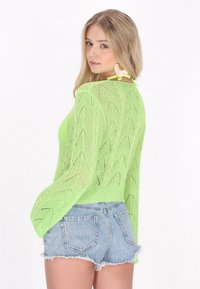 Grön stickad tröja i spetsmönster med en lös, öppen struktur, ihop med ljusblå slitna denim shorts med fransade kanter.