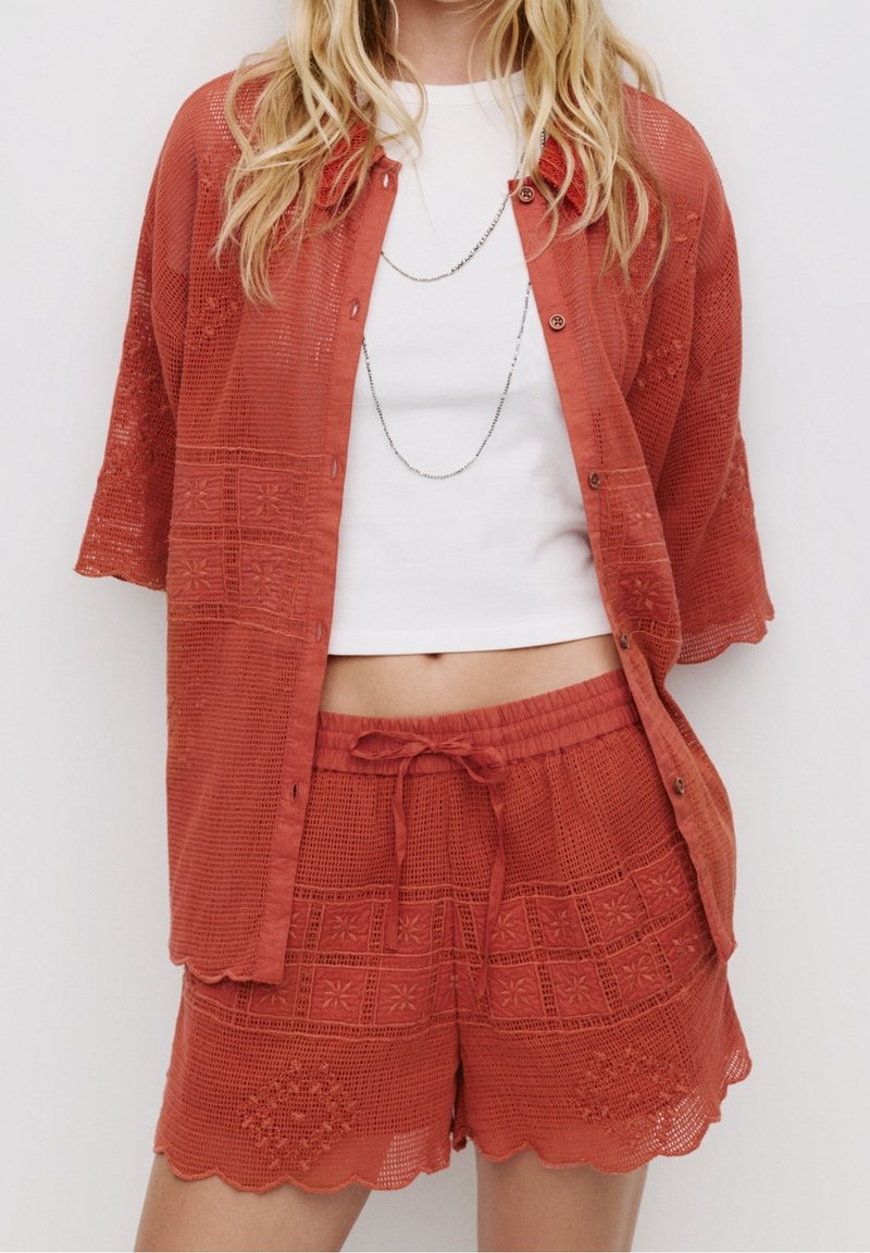 Ensemble en tissu tissé couleur rouille composé d'une chemise ample à boutons et d'un short assorti. Présente des motifs texturés et des ourlets festonnés.