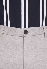 Pantalones grises texturizados con un botón negro en la cintura. La parte superior tiene rayas verticales en azul marino y blanco. Diseño simple y moderno.