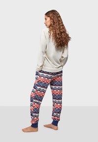 Loungewear set featuring a light-colored, long-sleeve top and patterned, soft pajama pants in red, navy, and white with heart motifs.