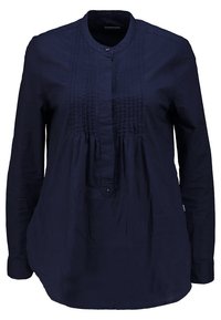Blouse bleu marine à manches longues avec col mandarin, patte boutonnée et plis piqués sur le devant.