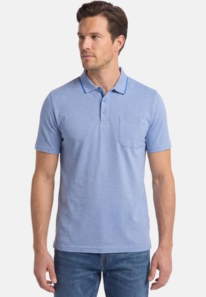 Man draagt lichtblauw poloshirt met korte mouwen, drie knopen en een borstzak, gecombineerd met een blauwe spijkerbroek, kijkt naar links.
