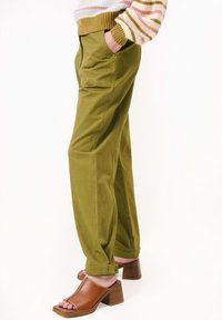 Olivově zelené bavlněné kalhoty s bočními kapsami a volným střihem, doplněné hnědými sandály na podpatku s širokým páskem a blokovým podpatkem.