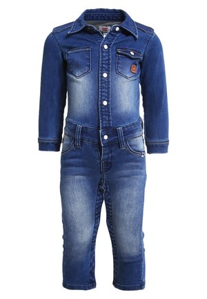 Combinaison en denim avec fermeture à boutons sur le devant, deux poches poitrine et un lavage bleu délavé. Manches longues et jambes fuselées avec détails de couture.