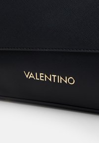 Borsa in materiale nero texturizzato con logo dorato "Valentino" sulla parte frontale. Design semplice con linee pulite e accenti minimalisti.